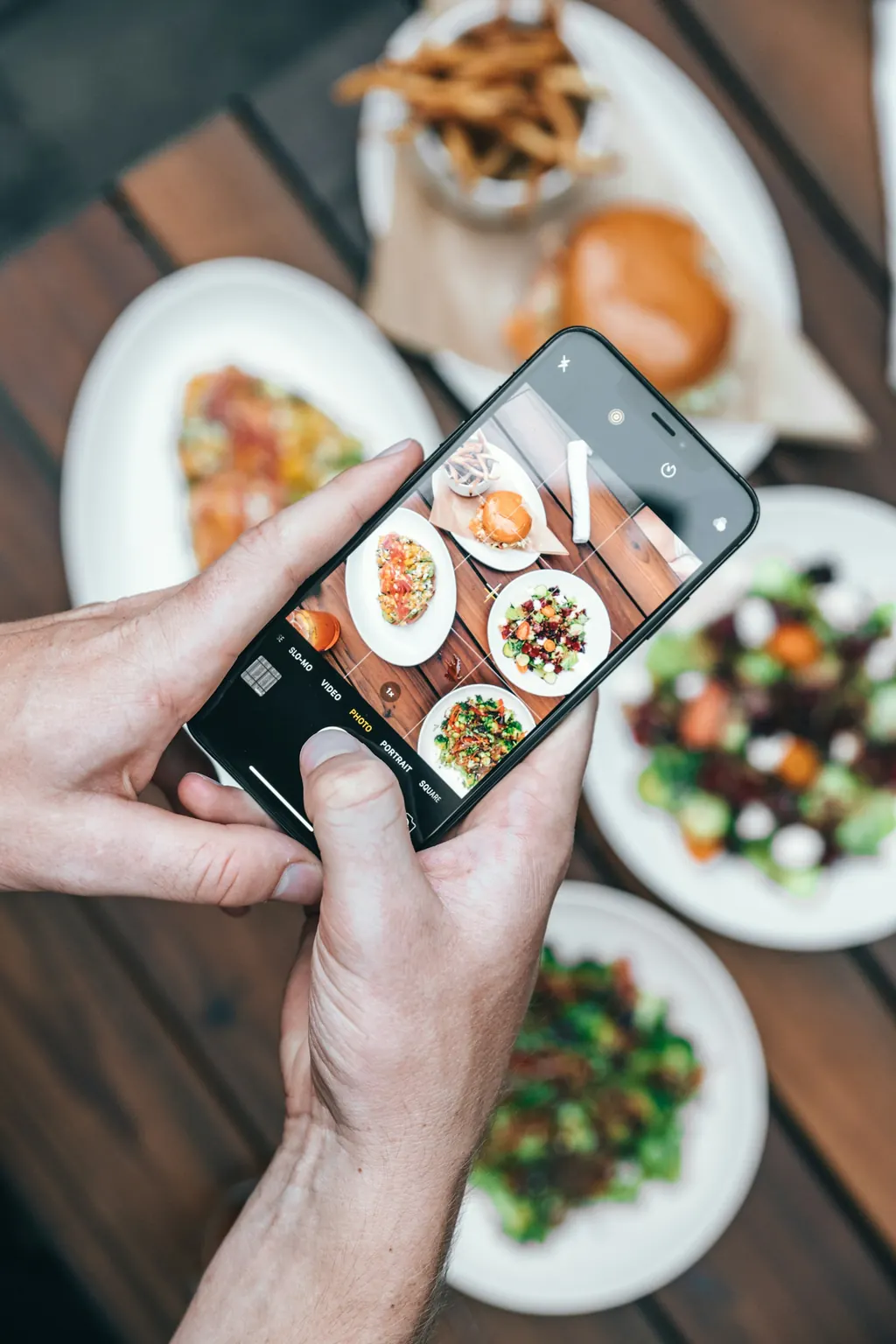 Hands photographing a table of shared dishes on a phone